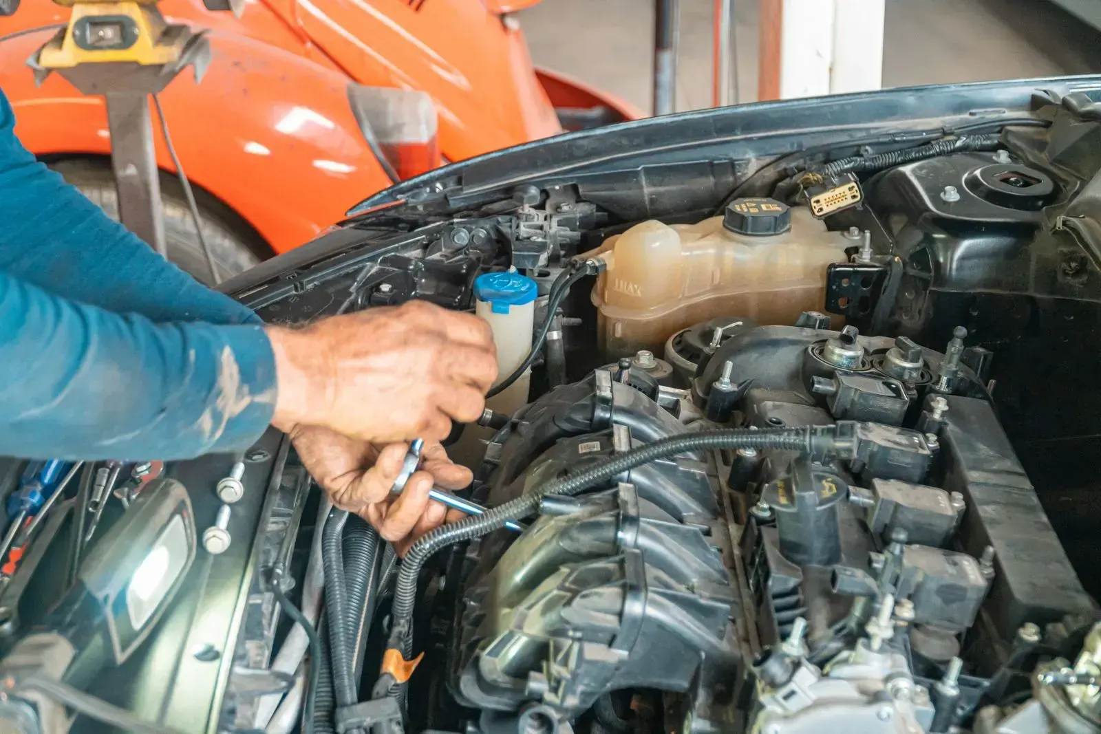 A hand reaching into an engine bay with a spanner.