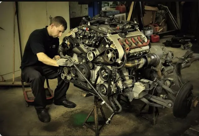 A mechanic working on an engine lifted out onto stands.